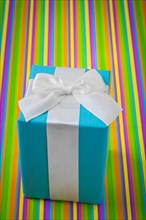Classic blue gift box with white ribbon on a striped coloured background