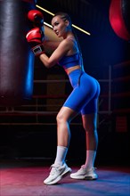Image of a powerful sportswoman boxer. She is posing near the bag against the background of the ring. The concept of wrestling and boxing. Mixed media