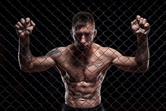 Dramatic image of a mixed martial arts fighter standing in an octagon cage. Powerful abdominal muscles. The concept of sports