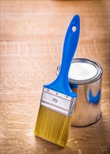 Brush with blue handle stands next to a tin on a wooden board