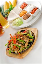 Original fajita sizzling smoking hot served on iron plate and fresh vegetables on background