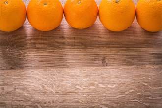 Five oranges organised in row on wooden board