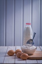 Eggs Flour scoop into bowl Bottle of milk on white lacquered old wooden board Eating and drinking concept