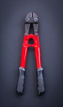 Aerial view of a red steel cutter with rubber handle on a black background