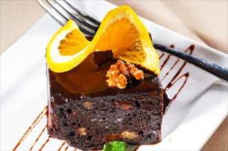 Fresh baked delicious chocolate and walnuts cake with slice of orance on top and mint leaf