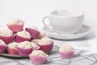 Coconut rum balls in pink moulds on a platter next to an empty coffee cup on a marbled surface