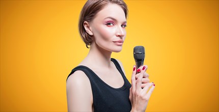 Portrait of an elegant stylish woman with a microphone. Yellow background. Karaoke concept.