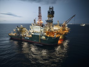 Brightly lit offshore drilling ship at dusk surrounded by calm sea