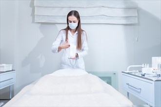The doctor is preparing to receive a patient in a beauty salon. The woman covers the couch with a protective hygienic white blanket.