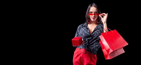 Beautiful sexy girl in glasses posing in the studio with red packages and a box for jewelry. Black background. Shopping concept.
