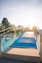 Blue pedestrian bridge over a swimming pool with a clear sky in the background