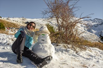 Latin woman sitting on frozen ground next to snowman