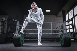 Athlete in a white sweatshirt put his foot on a barbell. Sports concept