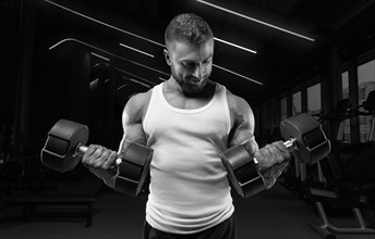 Muscular man in a white t-shirt works out in the gym with dumbbells. Biceps pumping. Fitness and bodybuilding concept.
