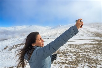 Latina woman taking a selfie with a smartphone while enjoying a winter day in sierra nevada