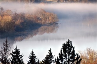 The Steinbach Dam near the national park community of Langweiler on the edge of the Hunsrueck-Hochwald National Park with fog on an early winter morning
