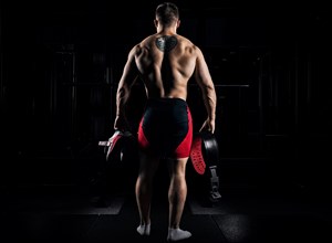 The athlete goes to the gym for training. In his hands he holds sneakers and a belt. Back view