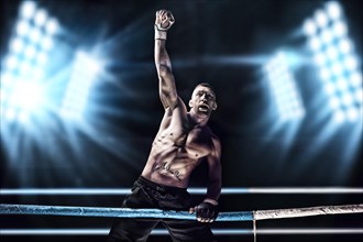 Kickboxer posing in the ring. The athlete climbed the ropes and took a victorious position against the background of spotlights. The concept of mma