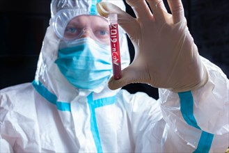 Doctor laboratory assistant in personal protective equipment against coronavirus holds a test tube with blood to perform a test for covid 19