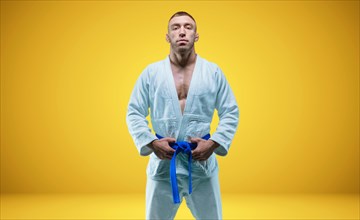 Strong man in a kimono with a blue belt. Yellow background. Martial arts concept.