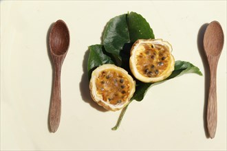 Passion fruits with wooden spoons and fresh leaves on a surface
