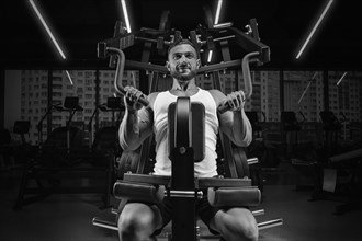 Image of a muscular guy in a white tank top on an exercise machine. Gym. Fitness concept
