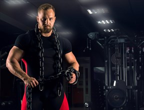 A strong athlete is wearing bench equipment with a chain around his neck against the background of sports simulators