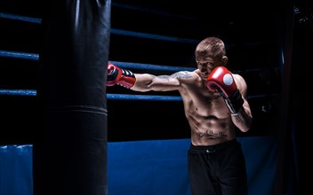 Professional boxer hits the bag against the background of the ring. Side view. The concept of sport and classic boxing.
