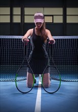 Portrait of a beautiful tennis player posing with two rackets on the court. Sports concept.