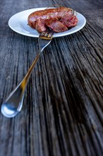 A Plate with Luganighe Sausage with a Fork on an Old Wood Table with Sunlight in Lugano