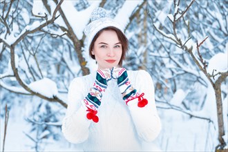 Portrait of a beautiful woman against the background of a winter forest in New Year's mittens. Concept of Christmas