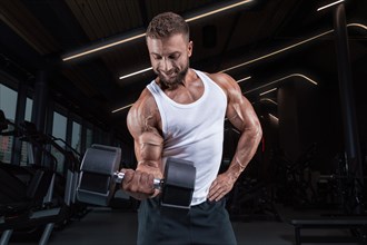 Image of a muscular guy in a white jersey with sports equipment. Gym. Fitness concept