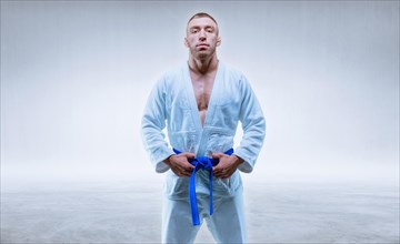 Athlete in a kimono with a blue belt stands on a light background. The concept of karate and judo.