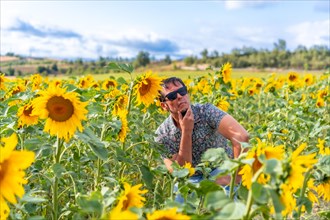 Thoughtful man with sunglasses among sunflowers enjoying summer