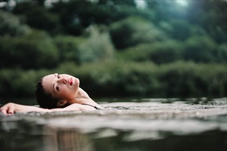 A young slender beautiful and hot girl with wet hair and big lips swims in the lake