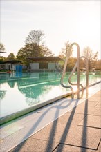 Sunlit stainless steel steps at the edge of a swimming pool with long shadows