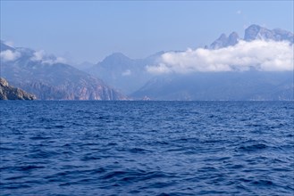 A calm seascape with mountains in the background and clouds in the sky