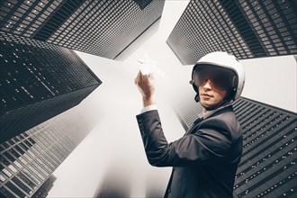 Portrait of a man in a suit and helmet. He launches a paper airplane up to the roofs of the skyscrapers of the financial district. Business concept.