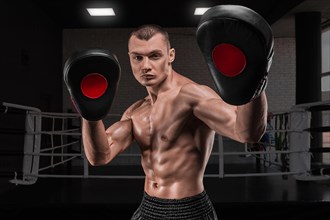 Brutal athlete holds boxing paws against the background of the ring. Mixed martial arts concept. High image quality