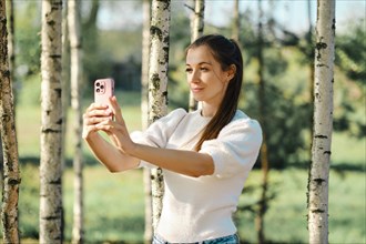 Influencer woman makes selfie on nature among birch trees