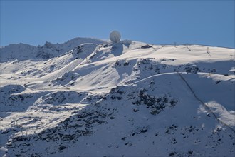 Snow-covered mountain under a clear blue sky with a radar antenna at the peak