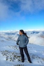 Middle-aged latina woman on a snow-capped mountain above the clouds