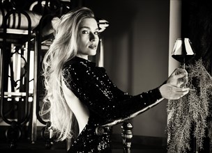 Seductive blonde in a green evening dress posing with a glass of red wine.