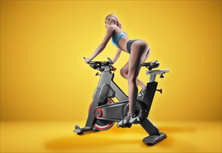 Long-legged girl posing in the studio on an exercise bike. Orange background. The concept of sports