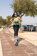 Young latina woman having fun with electric scooter by the beach