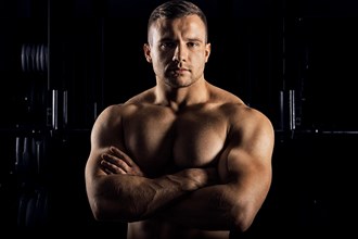 The weightlifter is posing in front of the camera with his arms crossed over his chest. Front view