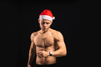 Sexy athletic man with a naked torso in a santa claus hat is preparing for a performance for christmas