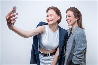 Portrait of two laughing women in blazers taking a selfie. Friendship concept.