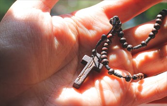 A hand holds a rosary with wooden beads and a cross