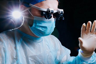 Surgeon wearing binocular magnifying glasses operates on a patient in a dark operating room